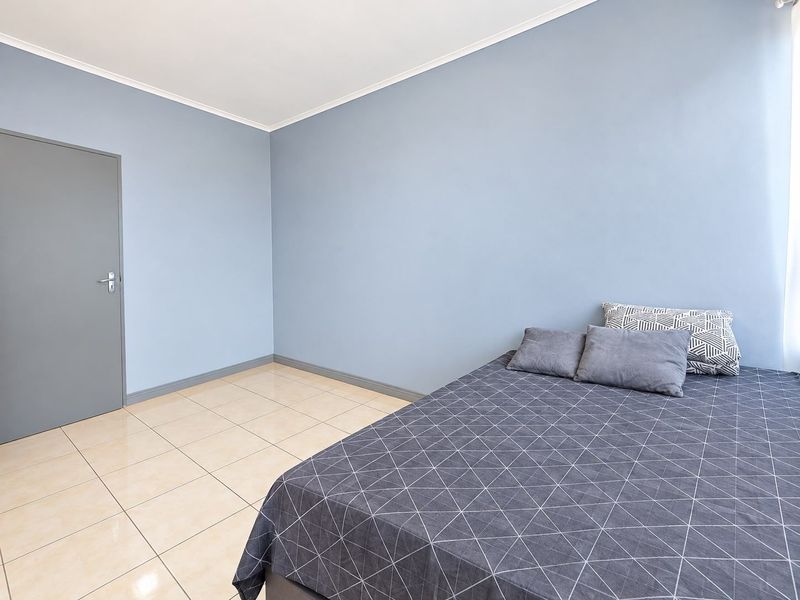 A well-maintained bedroom featuring light blue walls, neutral tiled flooring, and a coved ceiling, providing a clean and functional living space.