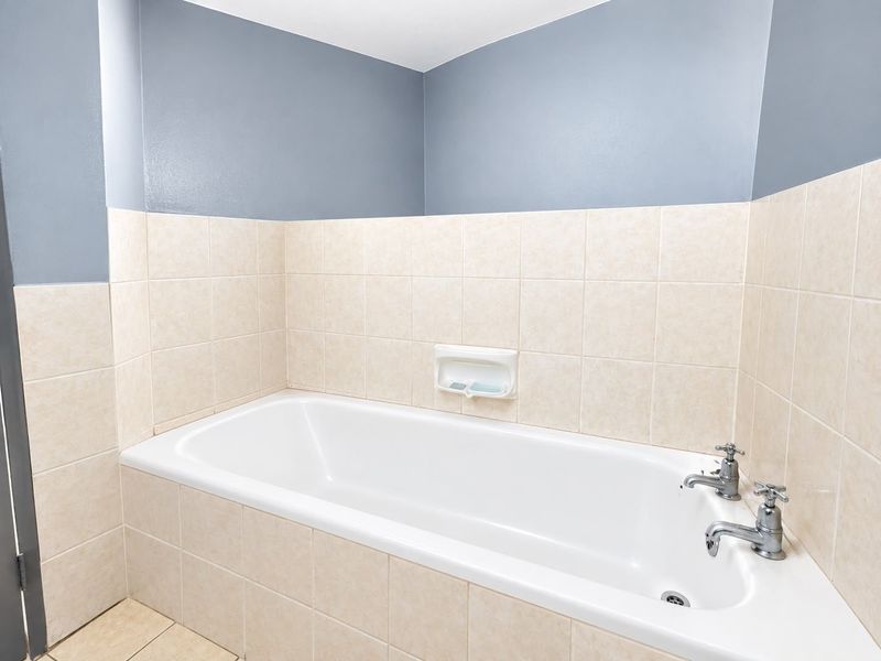 A clean, functional bathroom featuring a built-in bathtub with chrome fixtures and neutral ceramic wall tiling.