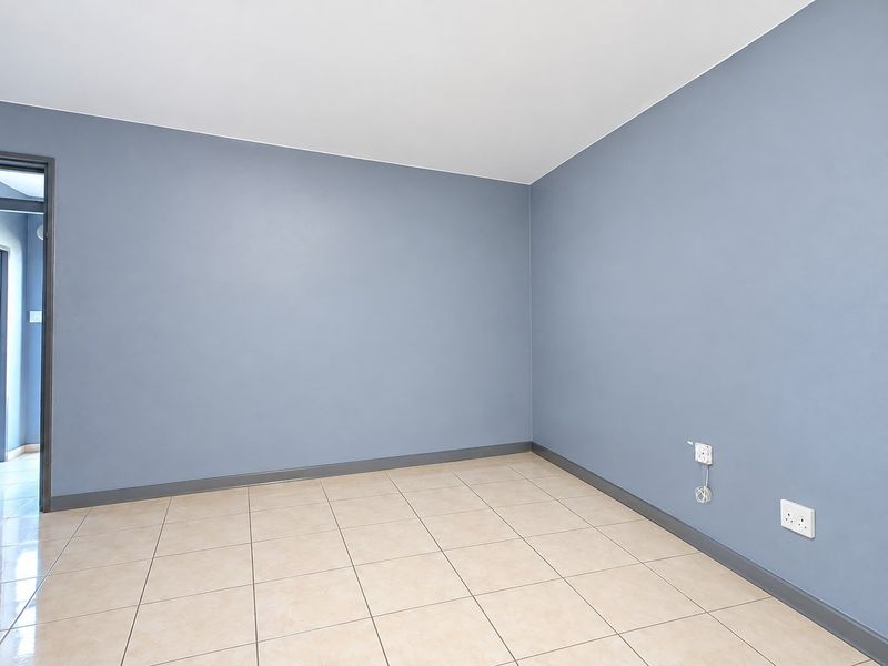 A clean, empty bedroom featuring neutral tiled flooring, blue painted walls, and dark grey skirting boards, ready for personalization.
