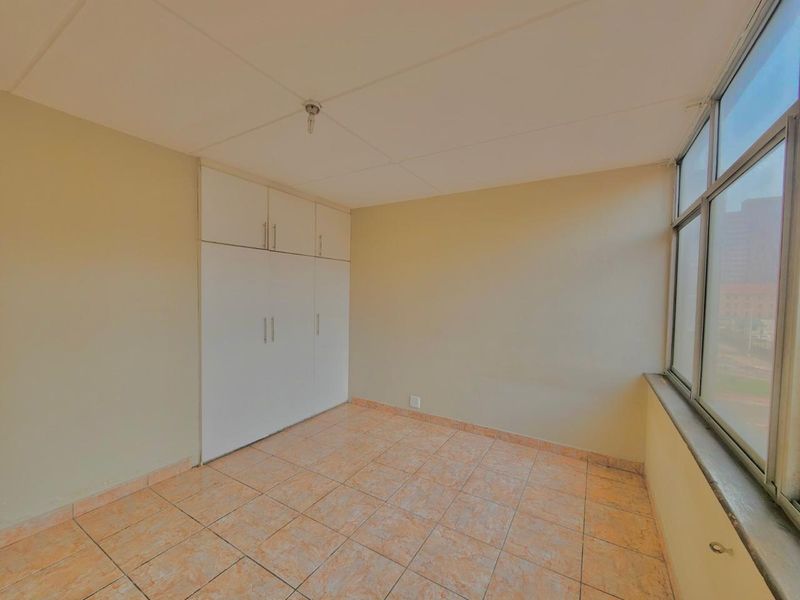 An empty bedroom featuring built-in cupboards, tiled flooring, and large windows providing natural light.