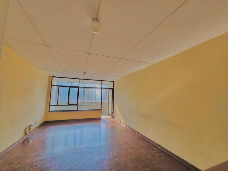 An empty living room featuring parquet flooring, large windows, and a tiled ceiling, offering a blank canvas for renovation and interior design.