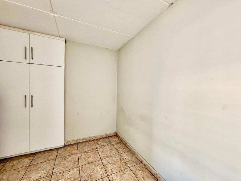 An empty bedroom featuring tiled flooring, a built-in wardrobe, and a drop ceiling, requiring minor cosmetic updates to the wall finishes.