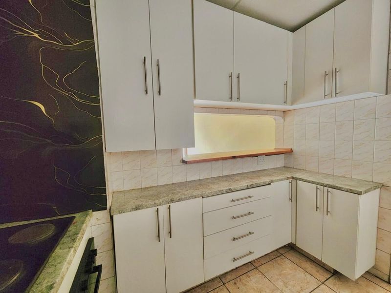 A functional kitchen featuring white built-in cabinetry, laminate countertops, tiled backsplash, and integrated cooking appliances, offering a clean and practical workspace.