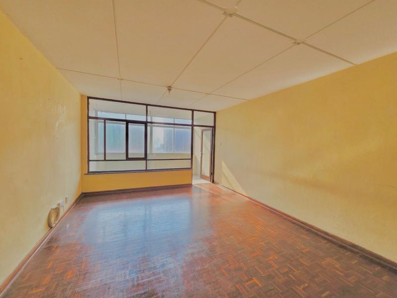 An empty living room featuring parquet flooring, large windows, and a tiled ceiling, offering a blank canvas for renovation and modernization.