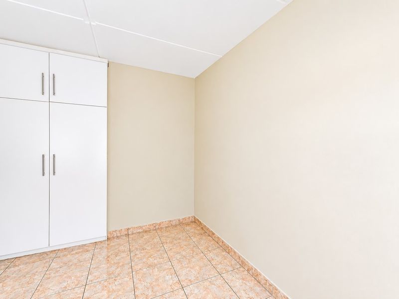 A clean, empty bedroom featuring neutral walls, tiled flooring, and white built-in cupboards, offering a blank canvas for personalization.