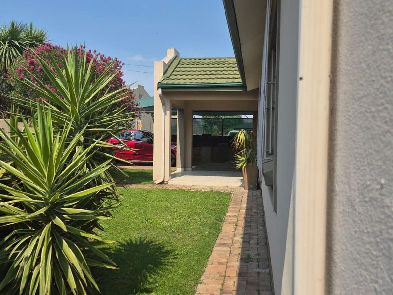 A view along the side of the house featuring a brick paved pathway, manicured lawn, and a covered rear patio area.
