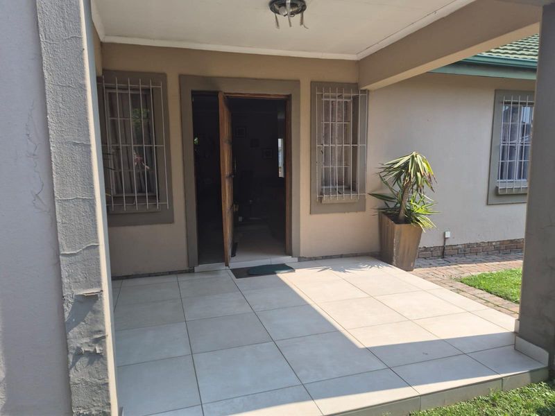 A covered patio area featuring tiled flooring and security bars on the windows, providing a functional outdoor entrance space.