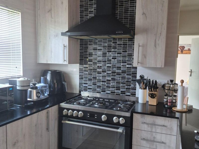 Modern kitchen featuring light wood-grain cabinetry, black granite countertops, a gas stove with extractor fan, and a decorative mosaic tile splashback.
