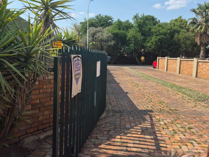 A view of the property entrance featuring a brick-paved driveway, perimeter brick walling, and a metal security gate.