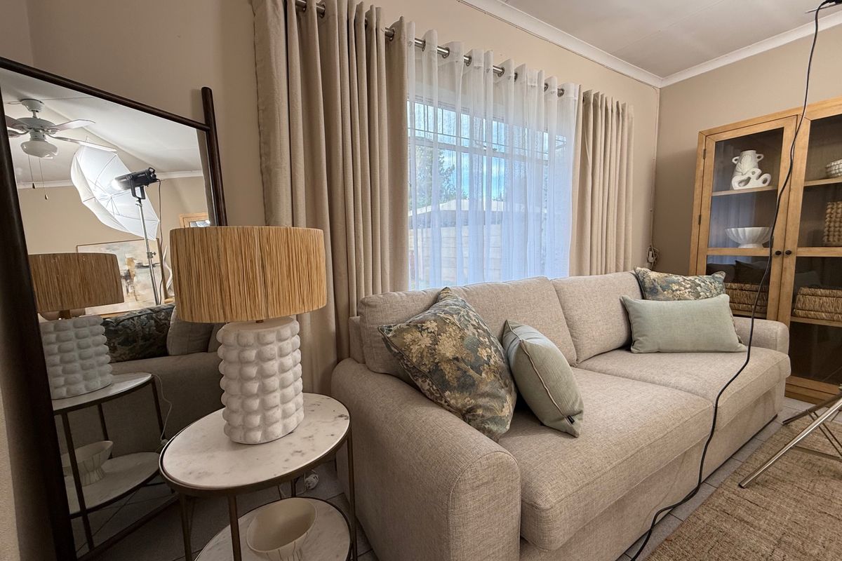 A comfortable living room featuring neutral tones, tiled flooring, and large windows with floor-to-ceiling curtains, creating a bright and inviting atmosphere.