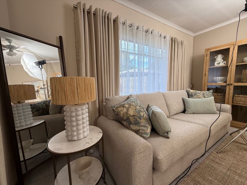 A comfortable living room featuring neutral tones, tiled flooring, and large windows with floor-to-ceiling curtains, creating a bright and inviting atmosphere.