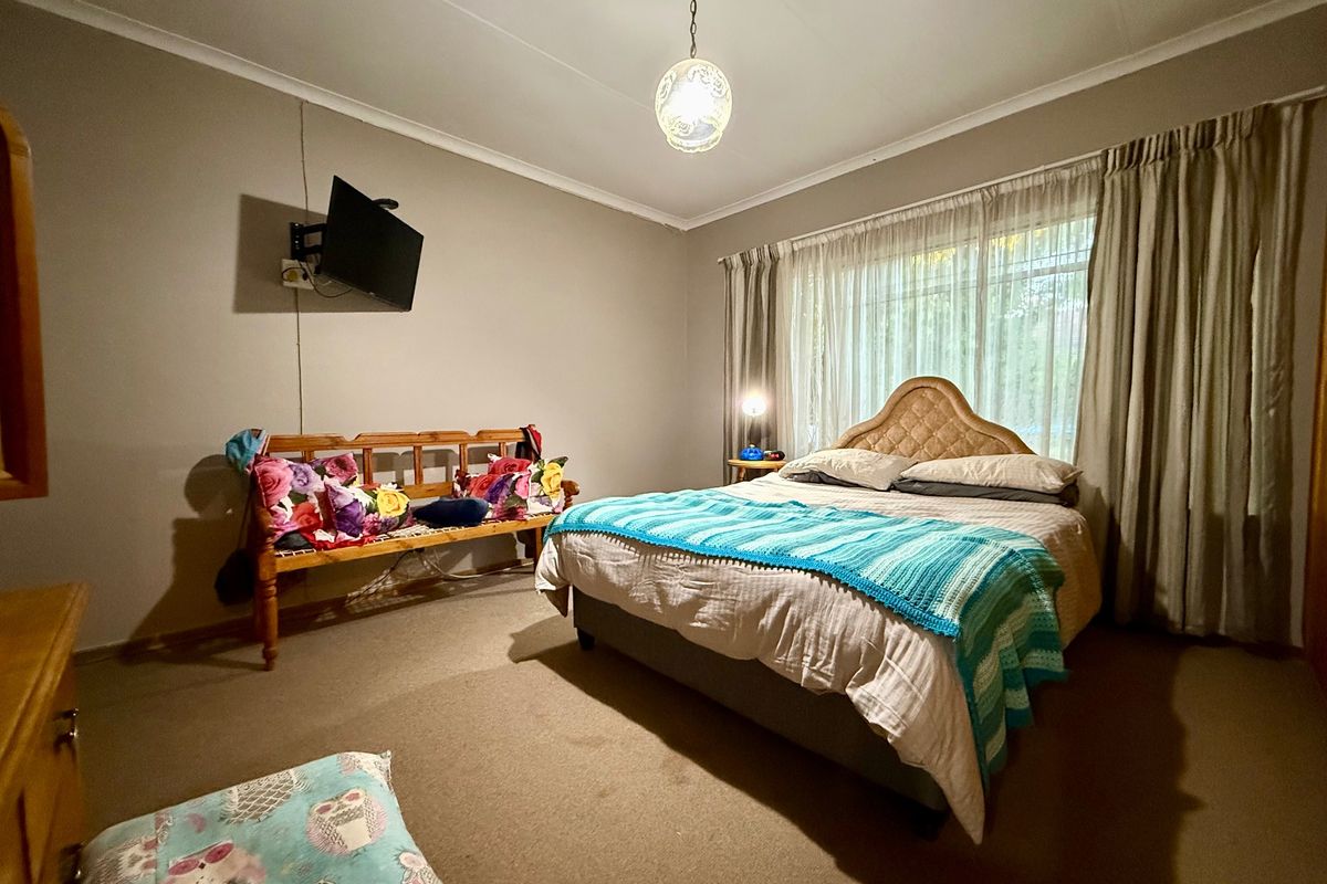 A standard bedroom featuring carpeted flooring, neutral wall finishes, and large window with curtain tracks.