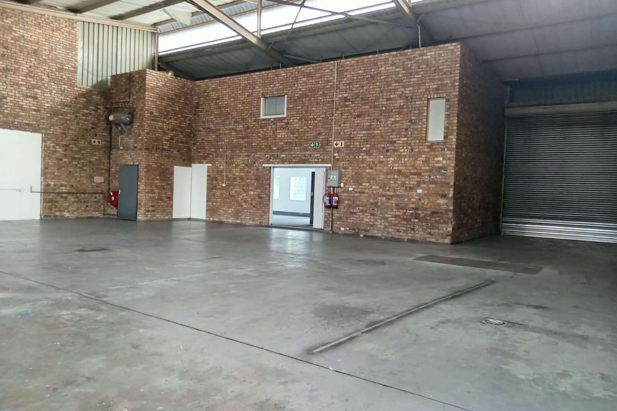 Spacious industrial warehouse unit featuring exposed brick walls, durable concrete flooring, high-clearance steel roof trusses, and a large roller shutter door for easy access.