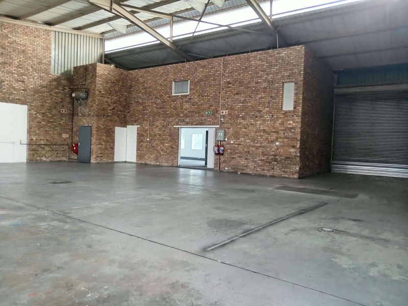 Spacious industrial warehouse unit featuring exposed brick walls, durable concrete flooring, high-clearance steel roof trusses, and a large roller shutter door for easy access.