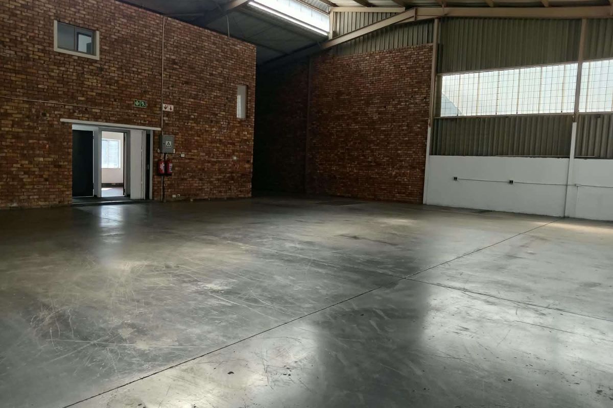 Spacious industrial warehouse unit featuring exposed brick walls, polished concrete flooring, and high-clearance steel roof trusses with natural light from clerestory windows.