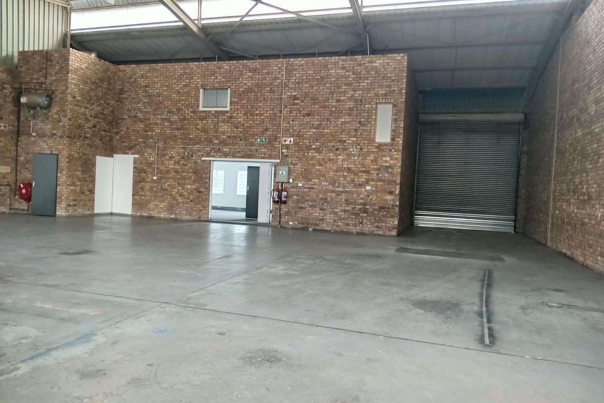 Spacious industrial warehouse unit featuring exposed brick walls, concrete flooring, high-clearance steel roof trusses, and a large roller shutter door for easy access.