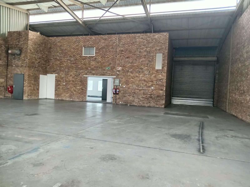 Spacious industrial warehouse unit featuring exposed brick walls, concrete flooring, high-clearance steel roof trusses, and a large roller shutter door for easy access.