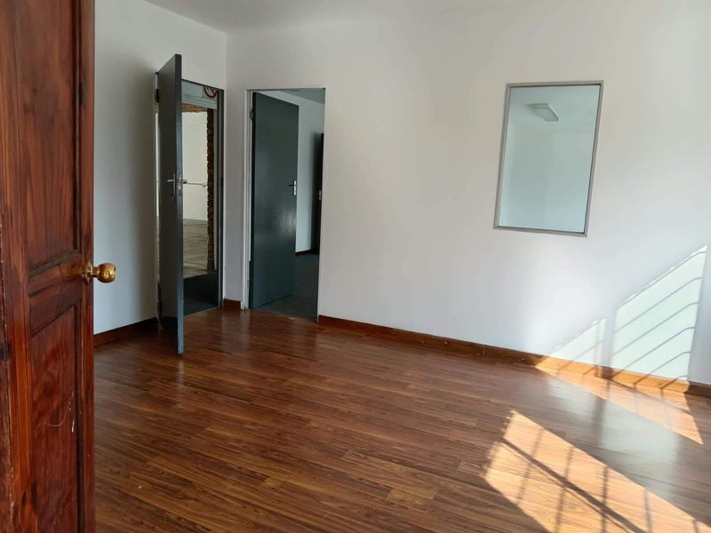 A bright, empty office space featuring warm-toned laminate flooring, white walls, and multiple internal access doors.