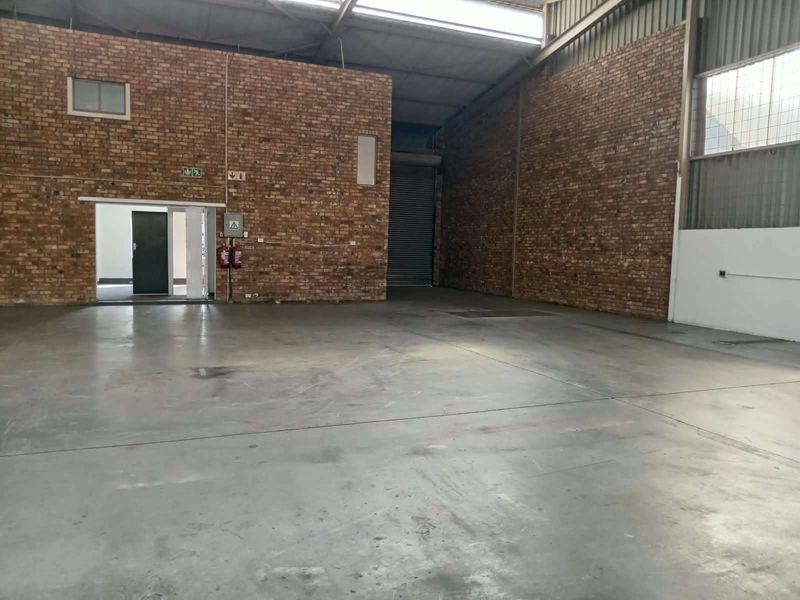 Spacious industrial warehouse unit featuring exposed brick walls, durable concrete flooring, and a large roller shutter door for easy access.