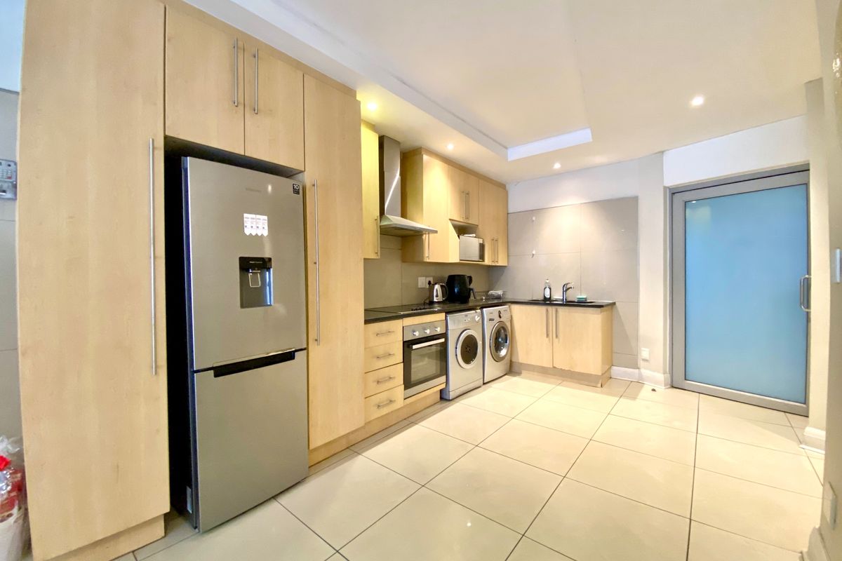 Modern kitchen featuring light wood cabinetry, integrated oven, extractor fan, tiled flooring, and a sleek frosted glass door leading to the exterior.