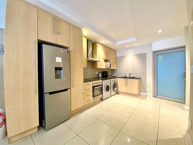 Modern kitchen featuring light wood cabinetry, integrated oven, extractor fan, tiled flooring, and a sleek frosted glass door leading to the exterior.
