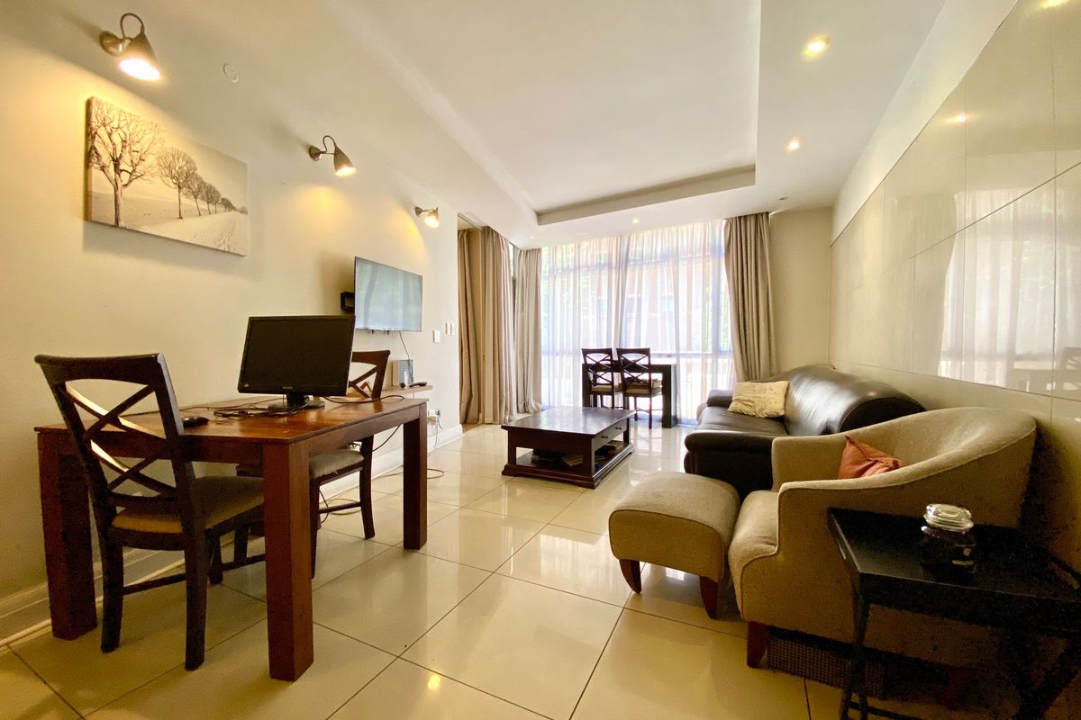 A well-lit living room featuring polished tiled flooring, recessed ceiling lighting, and large windows that provide ample natural light.
