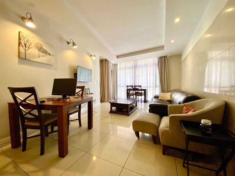 A well-lit living room featuring polished tiled flooring, recessed ceiling lighting, and large windows that provide ample natural light.