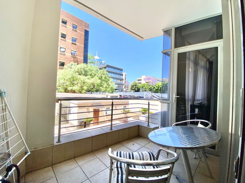 A covered balcony featuring tiled flooring and a stainless steel balustrade, offering an urban view of the surrounding neighborhood.
