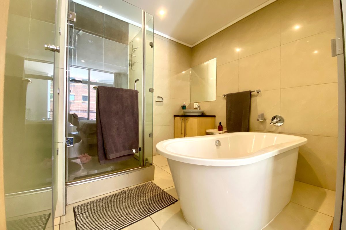 Modern bathroom featuring a freestanding bathtub, a separate glass-enclosed shower, and a vanity with a vessel sink, finished with neutral wall and floor tiles.