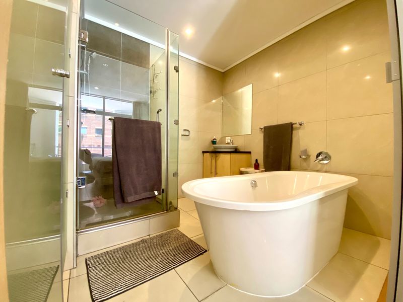 Modern bathroom featuring a freestanding bathtub, a separate glass-enclosed shower, and a vanity with a vessel sink, finished with neutral wall and floor tiles.