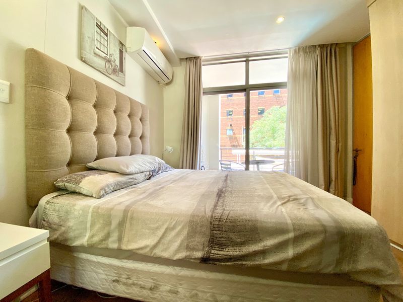 A well-lit bedroom featuring a split-system air conditioner, recessed lighting, and a sliding glass door providing access to a private balcony.
