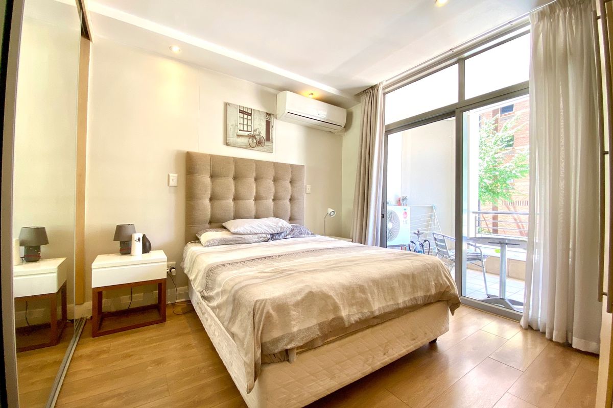 A well-maintained bedroom featuring laminate flooring, recessed lighting, a split-system air conditioner, and sliding glass doors providing access to a private balcony.