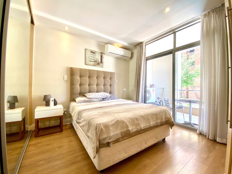 A well-maintained bedroom featuring laminate flooring, recessed lighting, a split-system air conditioner, and sliding glass doors providing access to a private balcony.