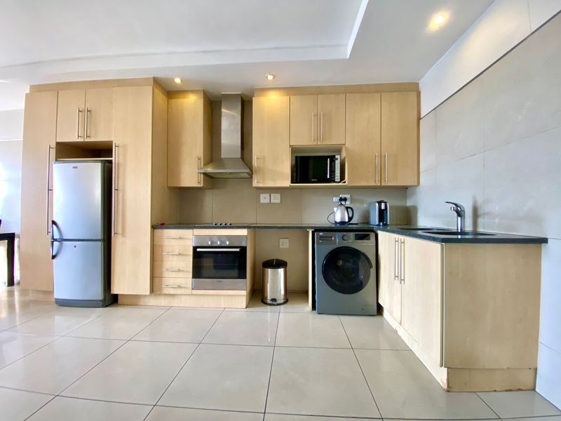 Modern kitchen featuring light wood cabinetry, stone countertops, integrated stainless steel appliances, and tiled flooring in an open-plan layout.