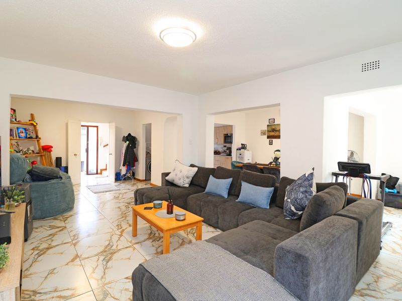 Spacious open-plan living area featuring marble-look floor tiles and neutral walls, providing a versatile layout that connects to the kitchen and entrance.