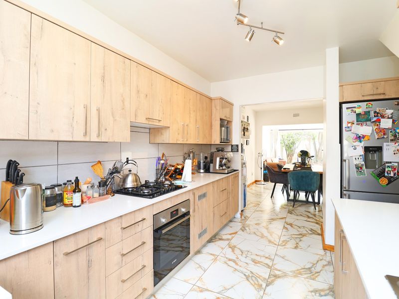 Modern kitchen featuring light wood cabinetry, white stone countertops, gas hob, built-in oven, and elegant marble-look floor tiles, flowing into the dining area.