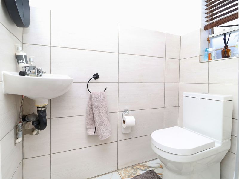 A compact bathroom featuring a wall-mounted basin, a standard toilet, and neutral wall tiling with a window for natural light.