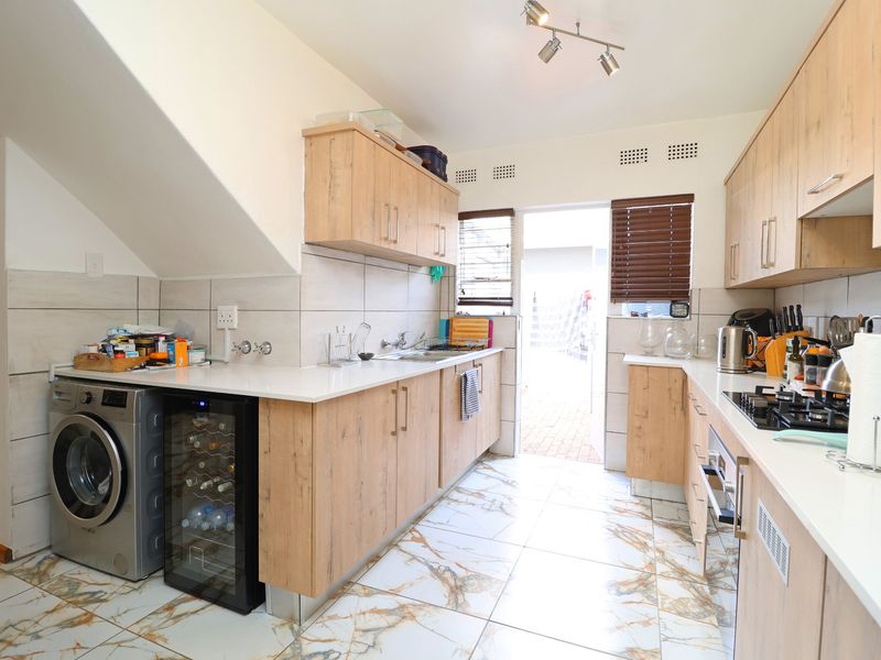 Modern kitchen featuring light wood-finish cabinetry, stone countertops, gas hob, built-in oven, and tiled flooring with direct access to the exterior.