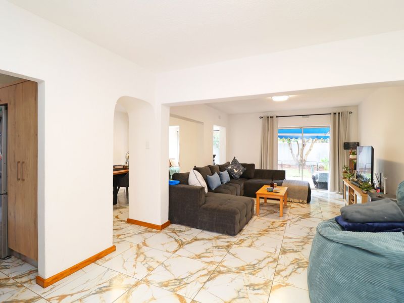 Spacious open-plan living area featuring modern marble-look floor tiles, an elegant archway, and seamless flow to the outdoor patio through sliding glass doors.