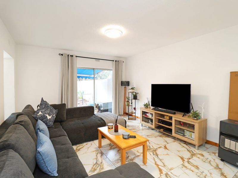 A bright living room featuring marble-look tiled flooring and a sliding glass door providing access to the outdoor patio area.