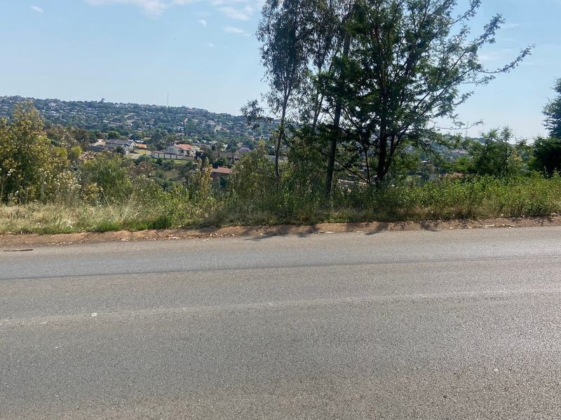 A view of the asphalt road frontage bordering the vacant residential land with surrounding neighborhood landscape visible in the background.