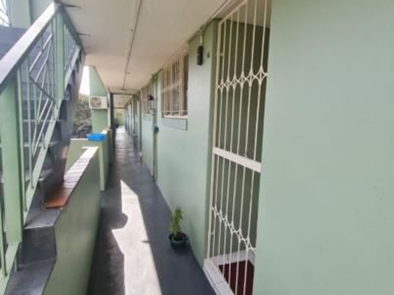 An exterior apartment hallway featuring a security gate, staircase access, and overhead lighting.