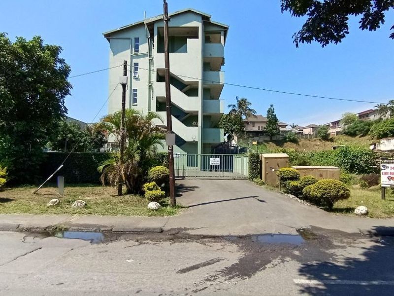 Front view of the apartment complex showing the gated entrance, driveway, and external staircase access.