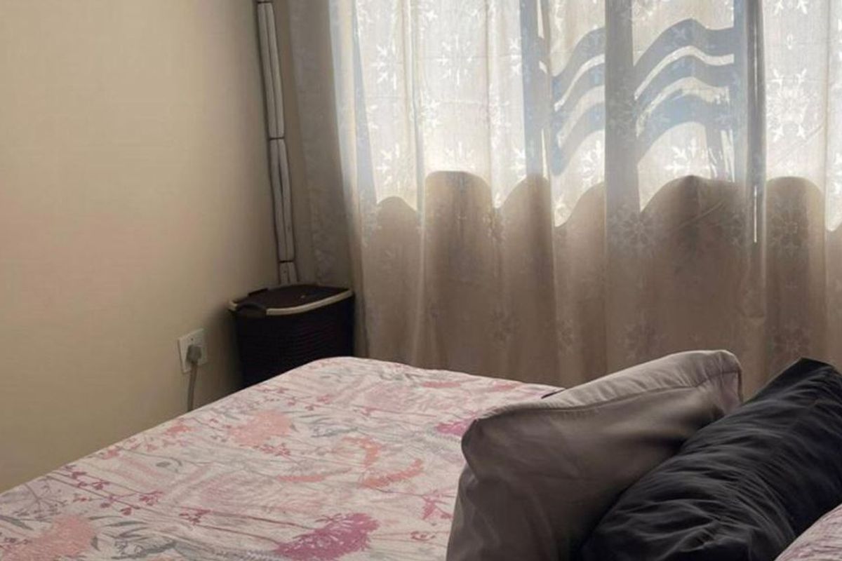 A bedroom interior featuring a window with curtains and a standard electrical outlet.