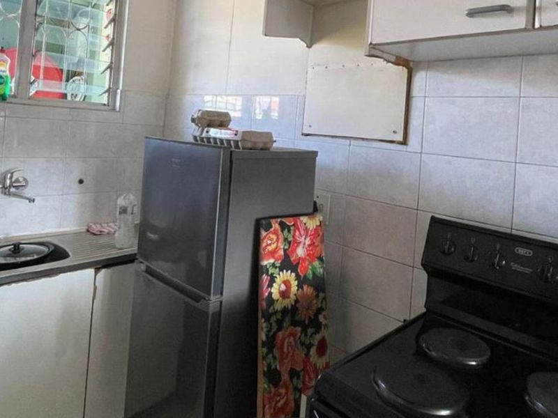 A functional kitchen featuring a stainless steel sink, tiled backsplash, and built-in cabinetry, requiring some cosmetic updates to improve its overall condition.