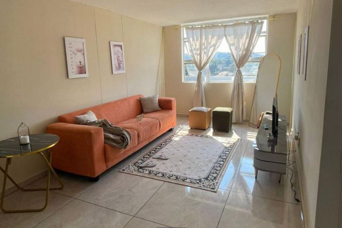 A living room featuring tiled flooring and a large window providing natural light, offering a functional space for relaxation.
