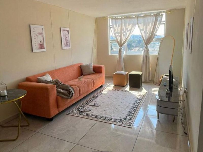 A living room featuring tiled flooring and a large window providing natural light, offering a functional space for relaxation.