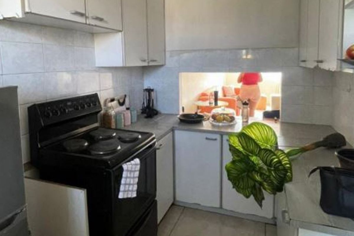A compact kitchen featuring white cabinetry, tiled backsplash, and a freestanding electric stove, with a serving hatch opening to the adjacent living area.