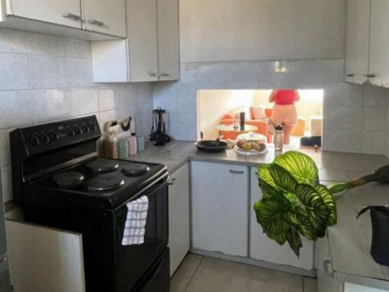 A compact kitchen featuring white cabinetry, tiled backsplash, and a freestanding electric stove, with a serving hatch opening to the adjacent living area.