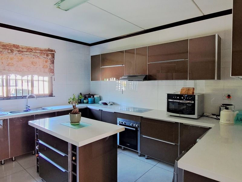 Modern kitchen featuring high-gloss cabinetry, a central island with stone countertops, built-in oven, hob, extractor fan, and tiled finishes throughout.